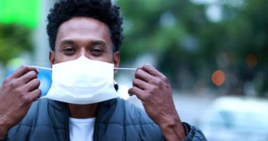 African man putting on pandemic mask prevention while walking in city forward