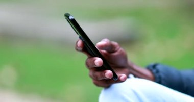 African hand holding cellphone scrolling online. Black person close-up checking smartphone