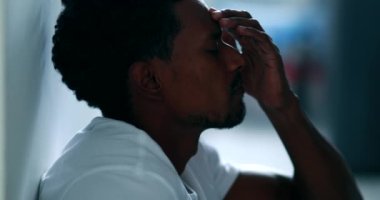 Black man feeling stress, african descent sitting on floor rubbing face with hand feeling worry and preoccupation, mental illness concept