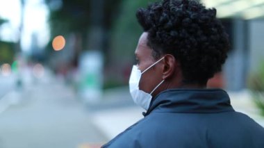 Back of black African man walking in city wearing covid mask in urban downtown walking in slow-motion