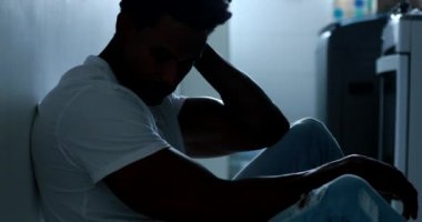 Silhouette of black man sitting on home floor in the shadows