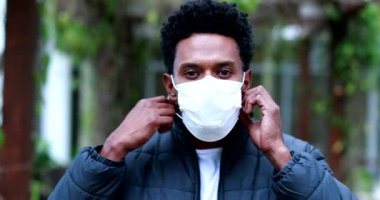 Black man removing covid virus mask outdoors looking to camera