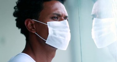 Thoughtful African man wearing covid mask during epidemic looking out window