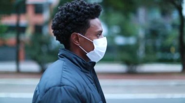 African american man walking in city wearing mask prevention. Profile of black man walking forward wearing covid-19 mask