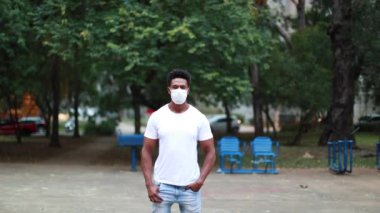 African black man standing wearing covid-19 surgical pollution mask at park outdoors, portrait looking to camera