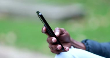 Close-up hand using smartphone, african black person checking cellphone outdoors