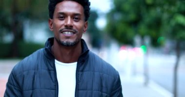 Confident African man walking forward in downtown city, portrait of smiling black person