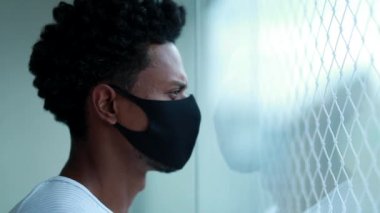 African american wearing covid mask prevention. Black man standing by window looking outside during epidemic outbreak