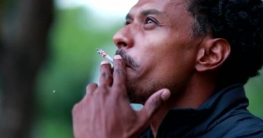 African man smoking cigarette outside, unhealthy habit