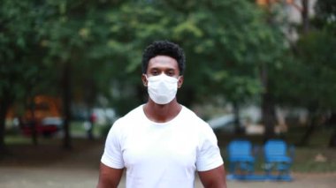 Black african person standing outside at park wearing mask against virus looking to camera