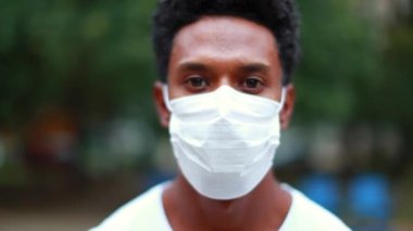Portrait of black african man wearing covid-19 surgical virus preventive mask outside looking to camera