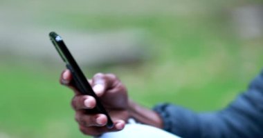 Young black man wearing covid mask during pandemic checking smartphone
