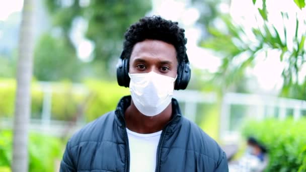 Young Black Man Wearing Surgical Mask Headphones Walking Camera — Stockvideo
