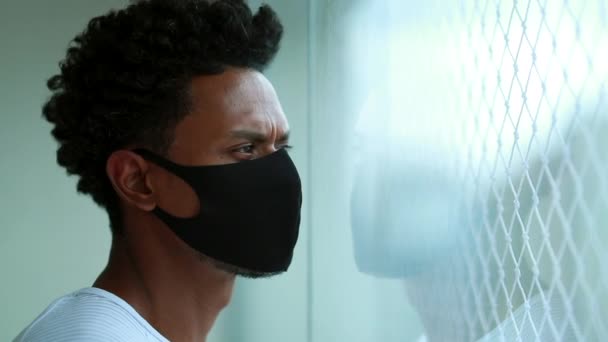 Μαύρος Αφρικανός Στέκεται Στο Παράθυρο Και Κοιτάει Έξω Φορώντας Μάσκα — Αρχείο Βίντεο