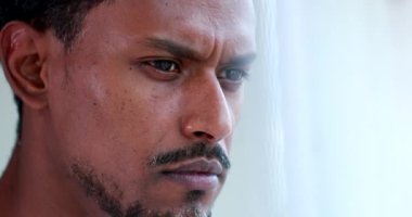 Concentrated serious African American descent thinking looking out window. Pensive close-up portrait face black man