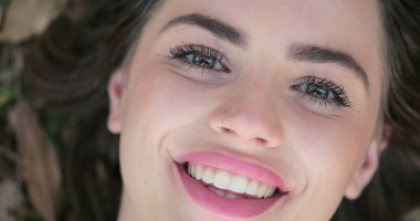 Pretty girl opens eye while laying down on grass at the park Woman with green eyes opening eyes looking to cameras