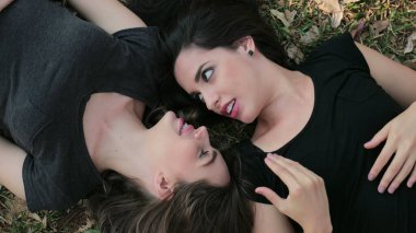 LGBT lesbian couple lay in a field daydreaming looking at each other smiling
