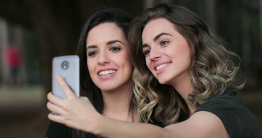 Friends together outside holding cellphone taking selfie at the park