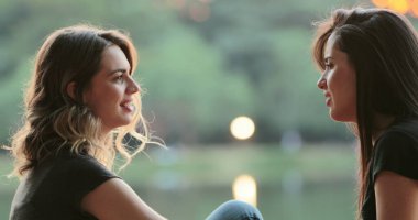 Friends gossiping and exchanging ideas in conversation outdoors in the sunlight by park lake