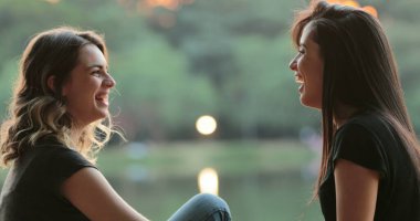 Friends gossiping and exchanging ideas in conversation outdoors in the sunlight by park lake