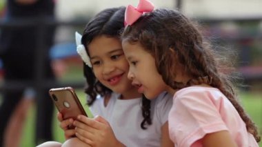 Children looking at cellphone at park. Two little girls pointing finger to smartphone screen