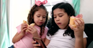 Kids eating sandwiches while looking at smartphone, children snacking while on social media