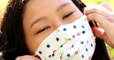 Asian young woman putting covid-19 face mask outside, looking at camera