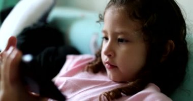 Child using laptop cellphone device. Little girl kid holding smartphone