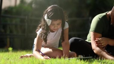 Hispanic little girl studying outside in grass, mixed race ethnically diverse child drawing