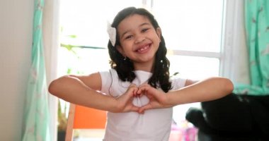 Cute little girl child making heart symbol to camera. Mixed race diverse kid