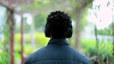 Back of black guy listening to music, podcast, or audiobook on headphones outside