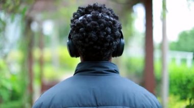 Back of person listening to audio using noise cancelling headphones outdoors