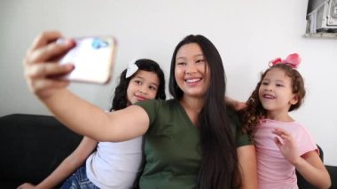 Asian mother holding cellphone taking selfie photo with little girls daughters