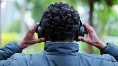 Young man putting on headphones over ears outside listening to music, podcast, or audiobook. Person wearing noise cancelling headphones outdoors