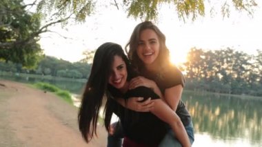 Girl piggy backing on friend back during sunset golden hour. Friends piggy back