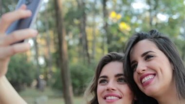Girlfriends taking a selfie together with cellphone at the park