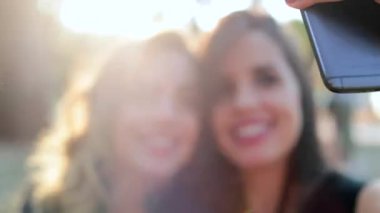 Female friends posing together taking selfie with cellphone outdoors