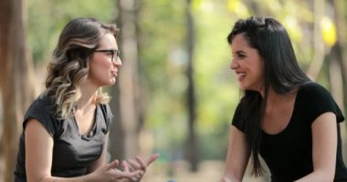 Girlfriends gossiping with each other at the park. Friends talking to one another outside