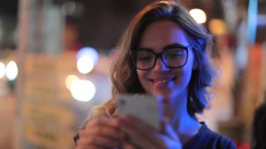 Woman using cellphone at night. Girl starring at smartphone screen in nightlife atmosphere