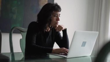 A pensive hispanic girl in front of laptop thinking. Thoughtful South American woman studying using computer
