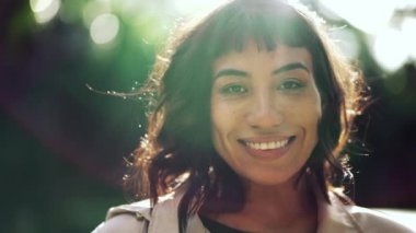 A young Brazilian woman smiling at camera sun flare. South American confident person standing outside