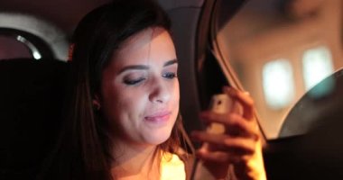 Passenger young woman checking and holding her cellphone while riding taxi at night