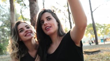 Female friends posing together taking selfie with cellphone outdoors