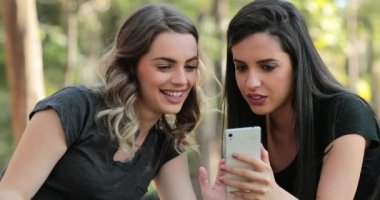 Authentic friends together outdoors checking cellphone. Girls looking and holding smartphone chatting exchanging gossip