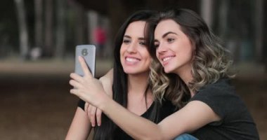 Friends together outside holding cellphone taking selfie at the park