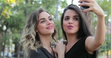 Two girlfriends holding cellphone posing for selfie