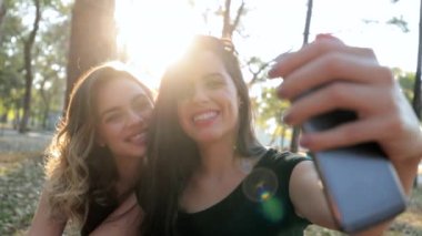 Female friends posing together taking selfie with cellphone outdoors