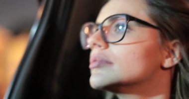 Passenger young woman with glasses looking out the window at night in the back seat of a taxi
