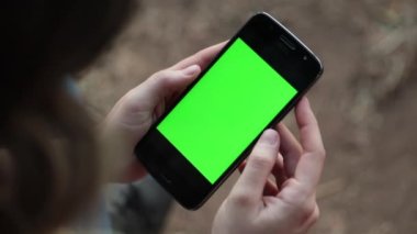 Person holding cellphone with green screen. Woman looking at smartphone with green-screen