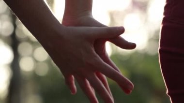 Arka planda güneş ışığının parlamasıyla birleşen ellerin yakın çekimi. İki aşık arasındaki güzel romantik an